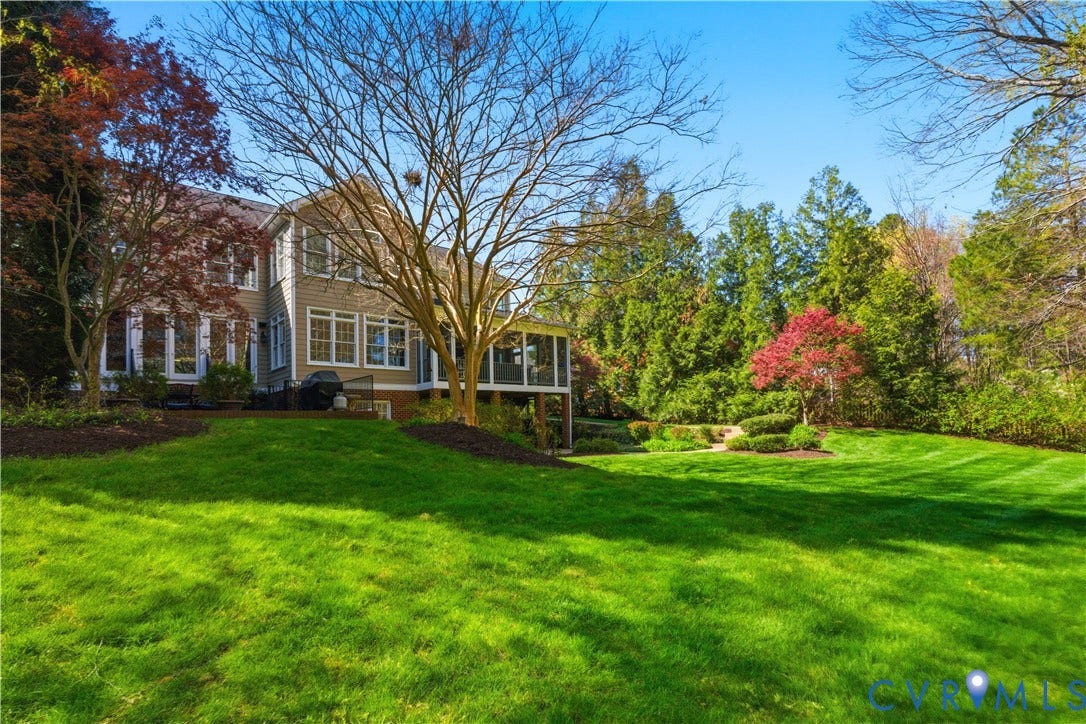 Expansive rear grounds featuring a manicured lawn, established landscaping, and mature trees
