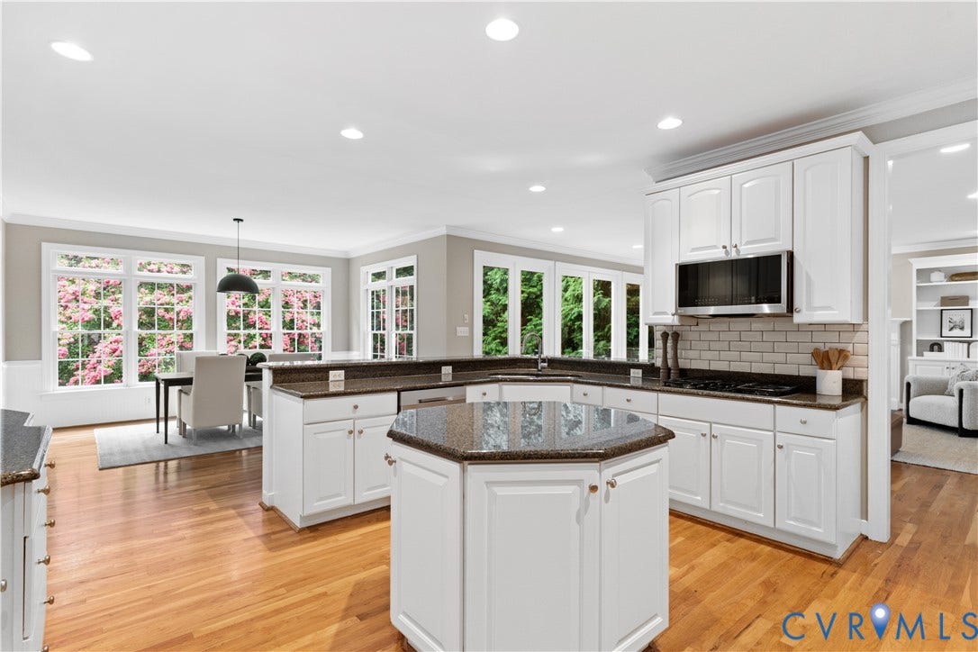 Kitchen featuring white cabinetry, dark granite countertops, stainless steel microwave, subway tile backsplash, and hardwood floors