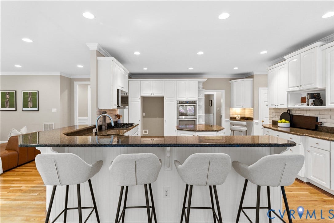 Spacious kitchen featuring an extended peninsula with seating, granite countertops, white cabinetry, integrated double ovens, and a subway tile backsplash