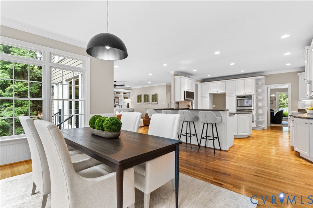 Spacious dining area with a modern pendant light and large windows, wood-finish flooring, white cabinetry, built-in stainless steel appliances, and an expansive kitchen island with a dark countertop