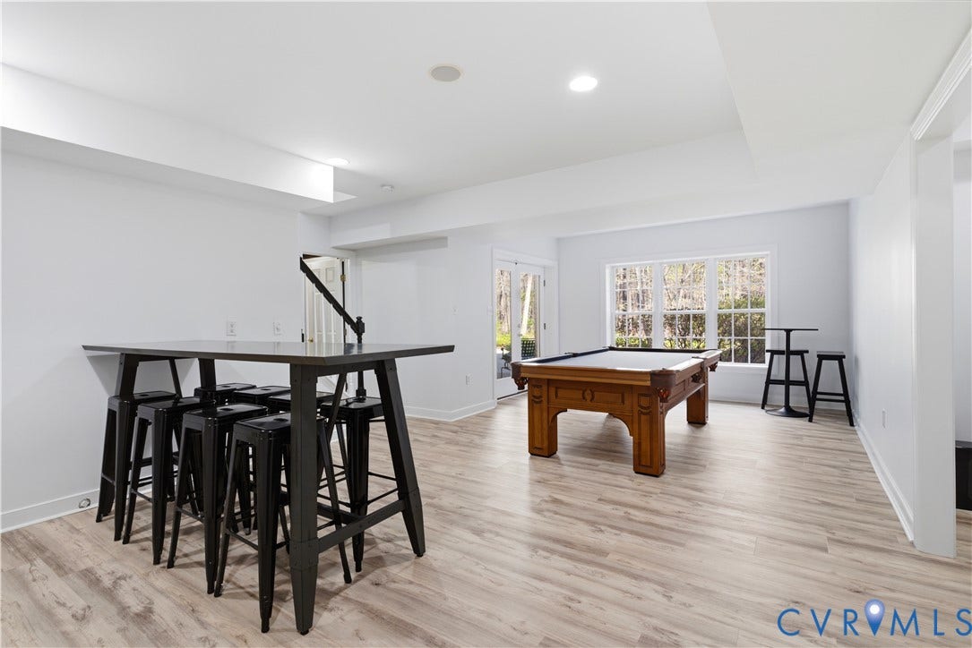 Spacious finished lower level featuring light wood-finish flooring (LVP), recessed lighting, and ample natural light from multiple windows and a glass-paned door