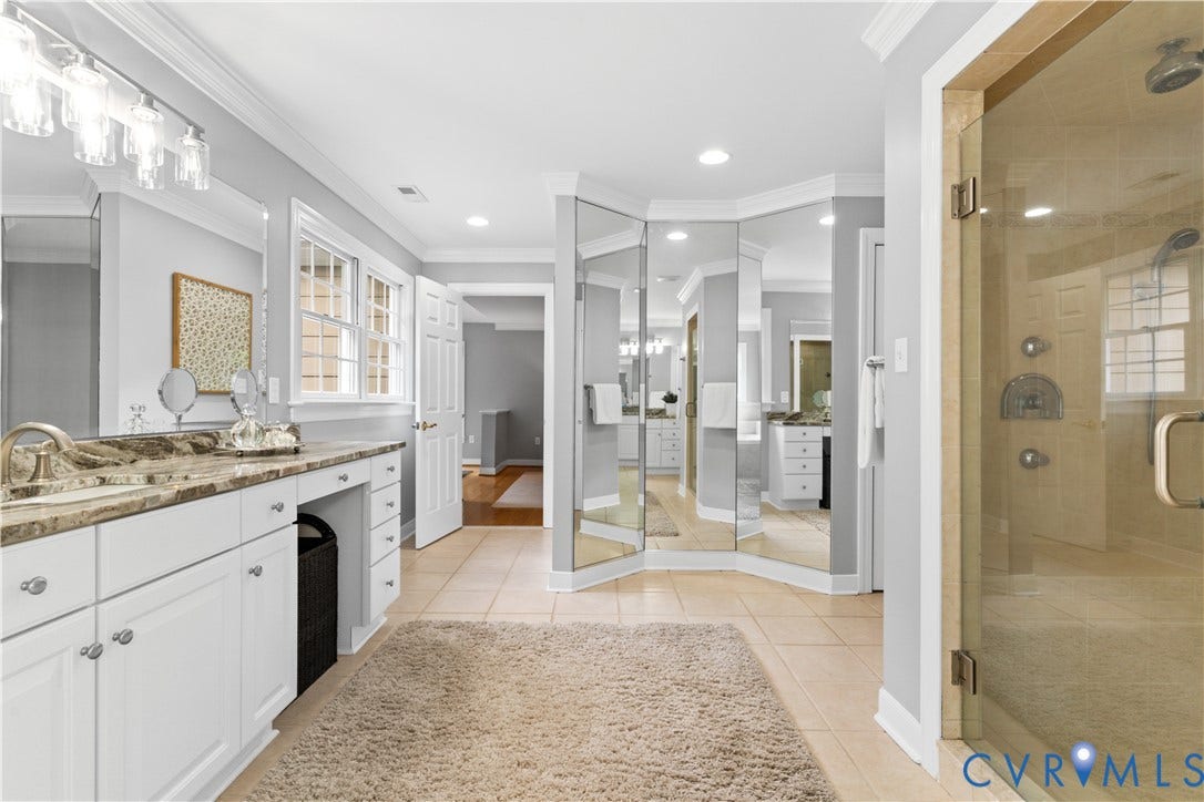 Spacious updated primary bathroom featuring a glass-enclosed shower, dual vanity with stone countertop, white cabinetry, tile flooring, and multiple windows