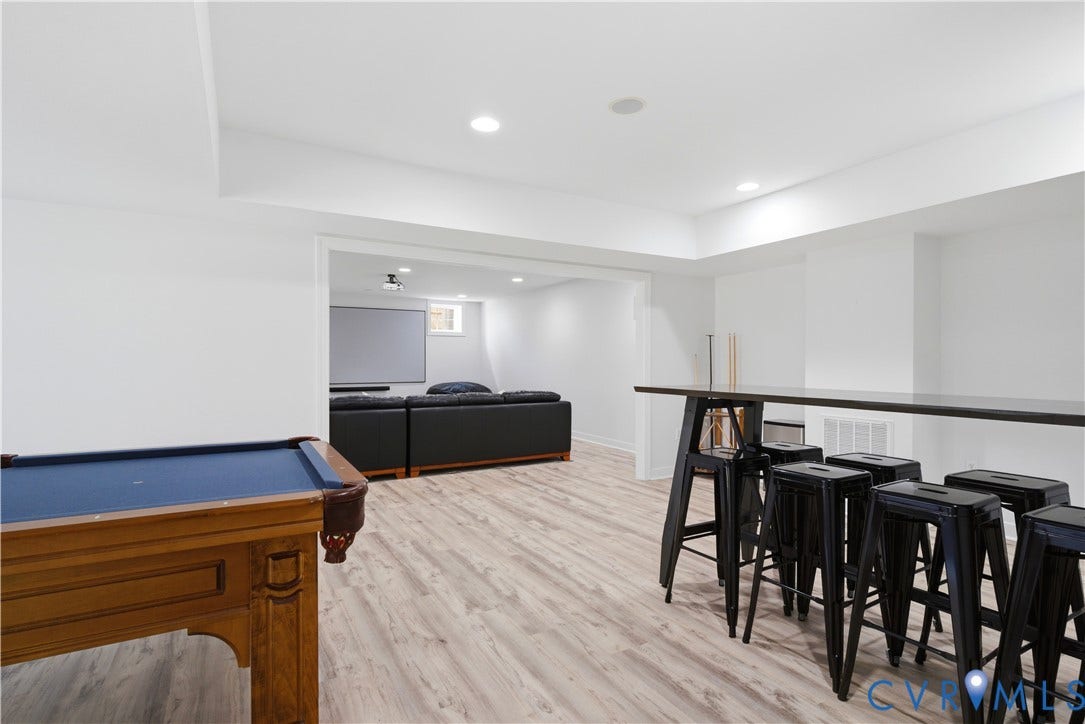 Newly renovated basement space. Plumbed for wetbar/kitchen, open-concept recreation area featuring wood-finish flooring (LVP), recessed lighting, a built-in projector screen, and a long bar with seating