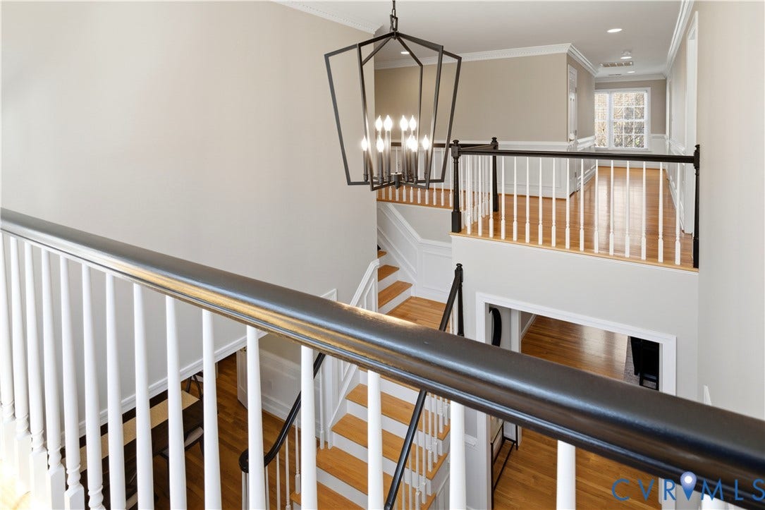 Multi-level interior featuring a contemporary modern, black chandelier, light wood-finish flooring, white spindle railings, and a contrasting black handrail