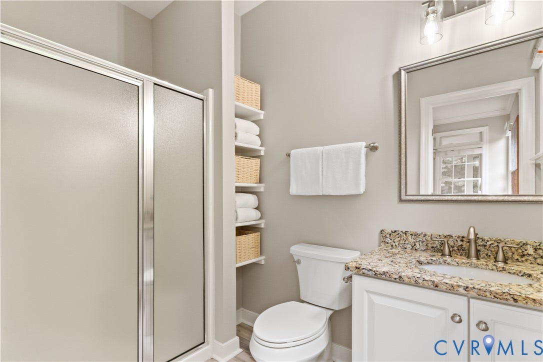 Bathroom featuring a glass-enclosed shower, built-in shelving, a vanity with a granite countertop, and wood-finish flooring