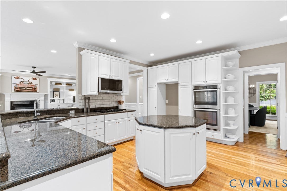 Kitchen featuring white cabinetry, granite countertops, wood-finish flooring, and stainless steel appliances including a double oven and microwave