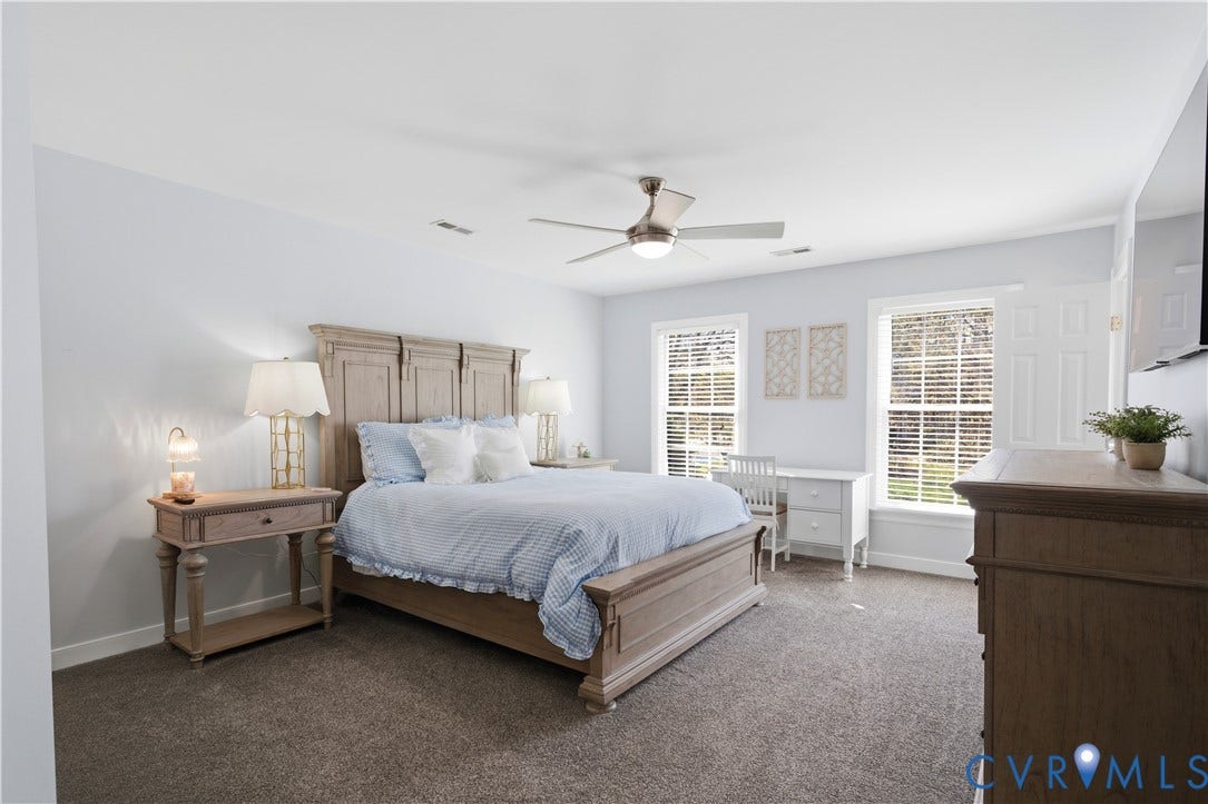 Spacious bedroom featuring light-toned walls, plush carpeting, and a ceiling fan with integrated lighting