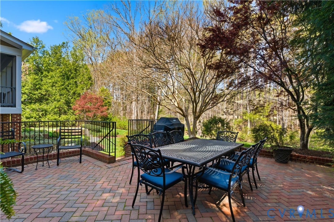 Expansive brick patio with herringbone pattern, surrounded by lush green foliage and mature trees