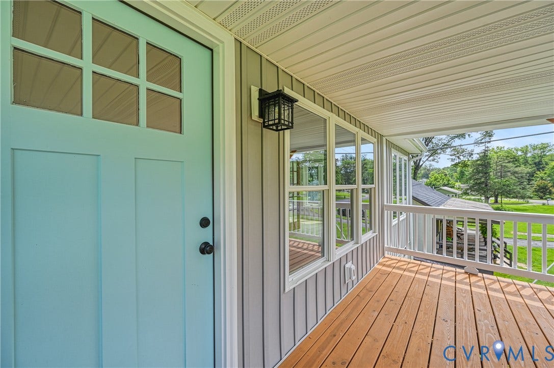 309 Ellis Drive, Louisa, VA 23093 Inviting front porch featuring a light blue entry door with clear glass panels, warm wood-finish flooring, white railing, grey vertical siding, and a black wall lantern