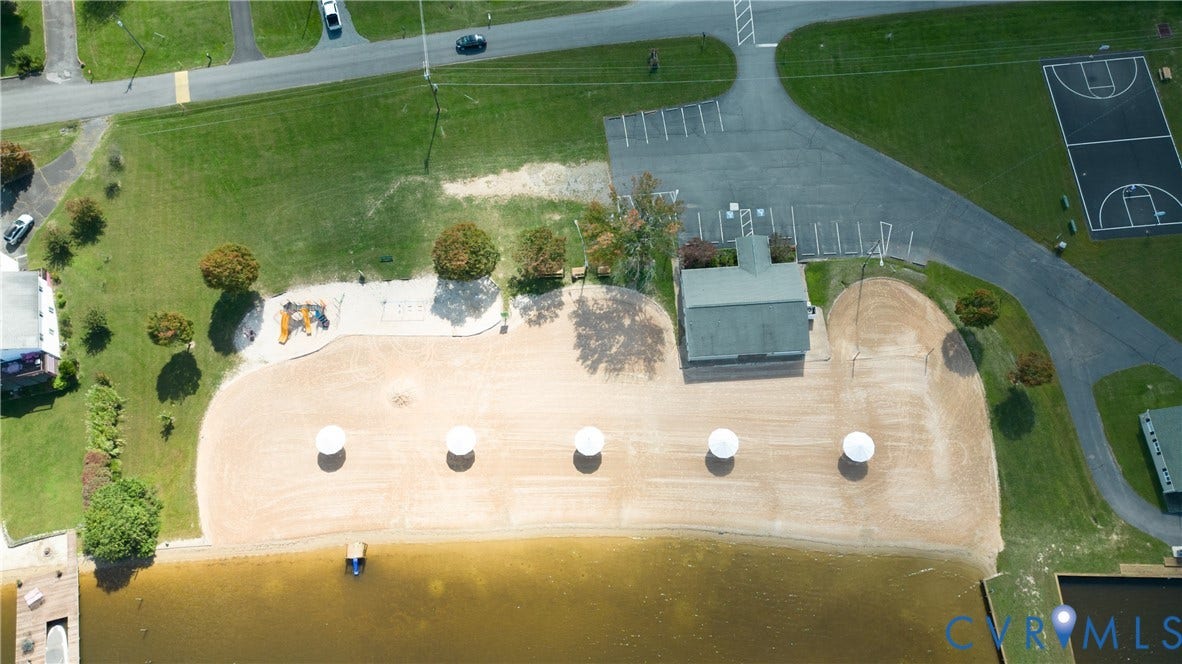 309 Ellis Drive, Louisa, VA 23093 Aerial overview showcasing a waterfront property featuring a sandy beach, a private dock, a recreational building, a paved parking area, and a basketball court