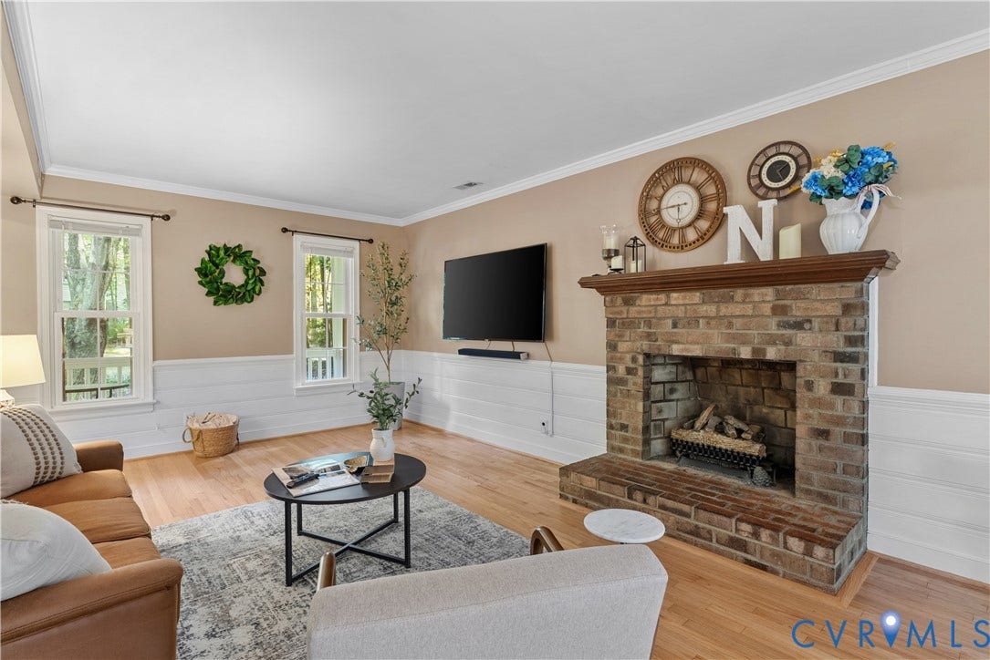 13908 Sterlings Bridge Road, Midlothian, VA 23112 Brick fireplace with a wood mantel, wood-finish flooring, white shiplap wainscoting, two windows, and crown molding