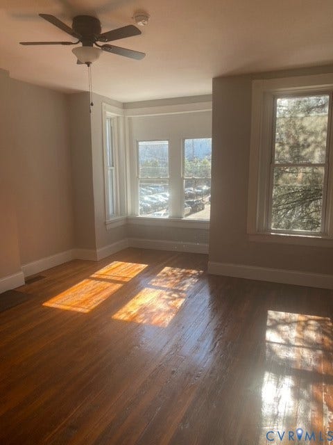 1100 W Marshall Street, Richmond, VA 23220 Spacious room featuring wood-finish flooring, a ceiling fan with integrated lighting, and multiple windows including a bay window for ample natural light