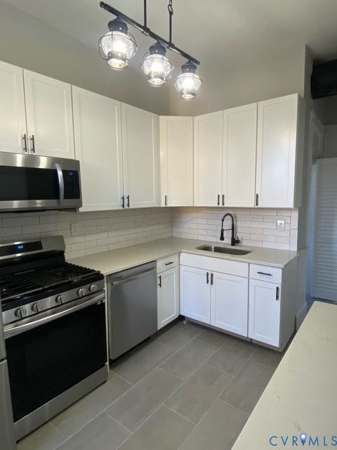 1100 W Marshall Street, Richmond, VA 23220 Corner kitchen featuring white shaker cabinetry, stainless steel appliances including a gas range and built-in microwave, light-toned countertops, subway tile backsplash, and a modern track light fixture