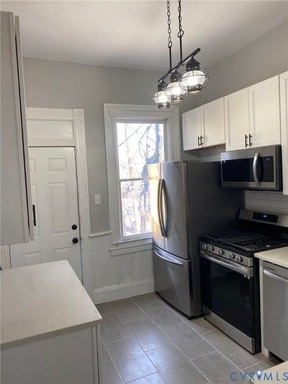 1100 W Marshall Street, Richmond, VA 23220 Kitchen featuring white shaker cabinetry, stainless steel appliances, light-toned countertops, tile flooring, and a multi-bulb pendant light fixture