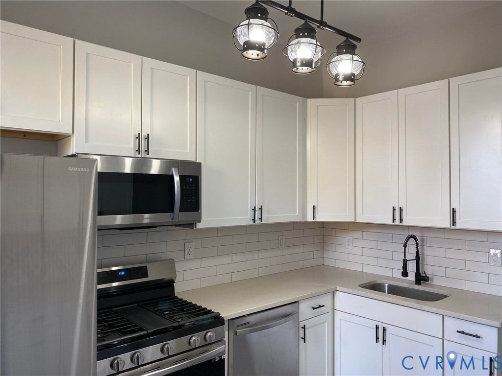 1100 W Marshall Street, Richmond, VA 23220 Modern kitchen featuring white shaker cabinetry, stainless steel appliances, light-toned countertops, subway tile backsplash, and a contemporary track light fixture