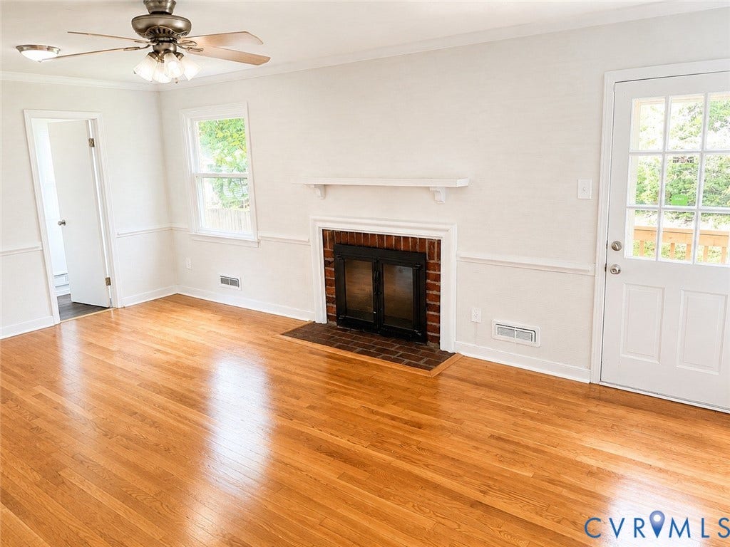 10250 Epsilon Road, Southwest, Richmond, VA 23235 Bright interior featuring polished wood flooring, a brick fireplace with a white mantel, and a multi-pane glass-insert door