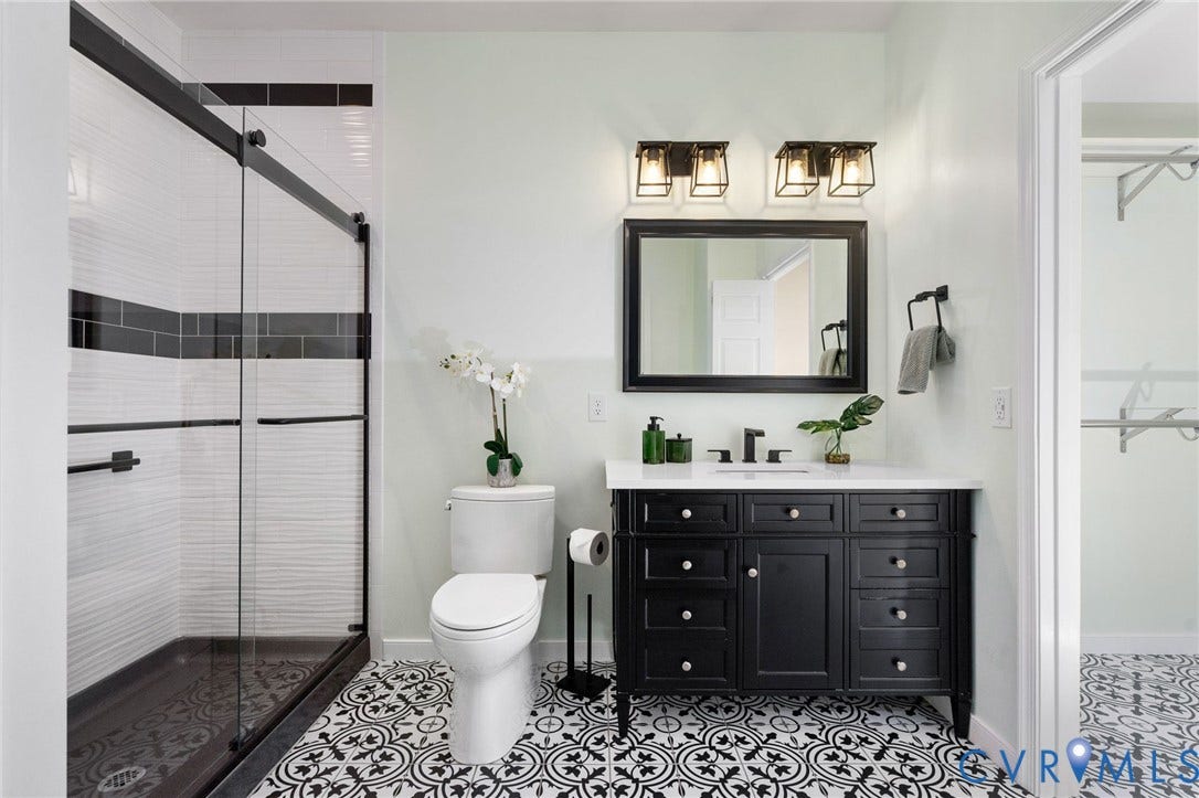 5806 Park Creste Drive, Glen Allen, VA 23059 Bathroom featuring a black vanity with a white countertop, patterned floor tiles, a glass-enclosed shower with black trim, and wall-mounted lighting fixtures