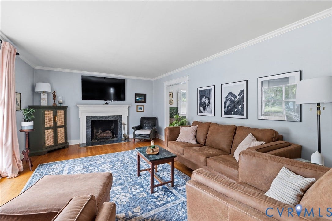 Living area featuring wood-finish flooring, crown molding, a built-in fireplace with a stone surround and mantel, and light blue wall tones
