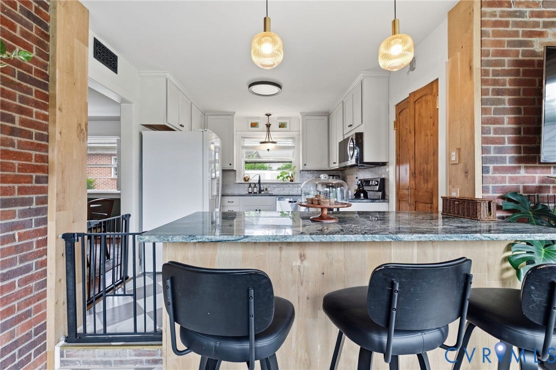Kitchen featuring an eat-at island with a light-toned wood-finish base, granite countertop, light cabinetry, and stainless steel appliances