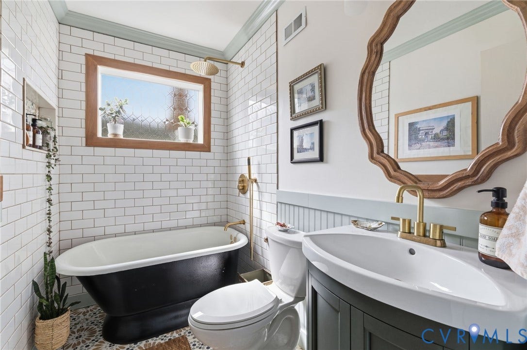 Bathroom featuring a freestanding black bathtub with brass fixtures, white subway tile walls, a wood-framed window, and a mosaic floor