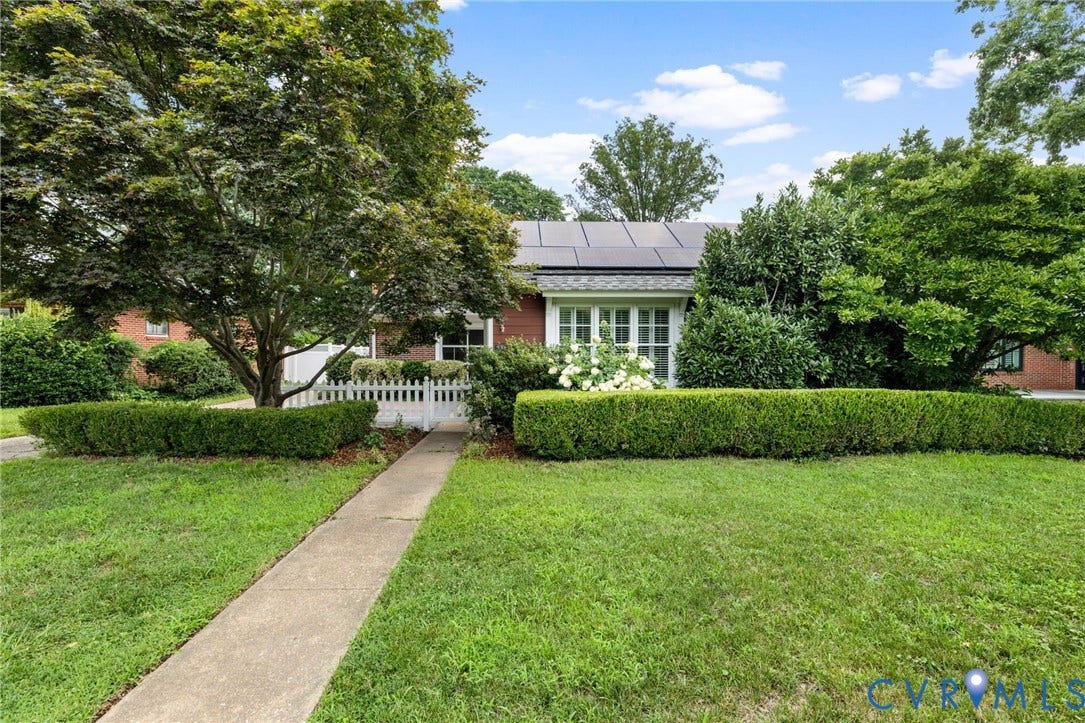 Brick exterior residence featuring a white picket fence, mature trees, and solar panels