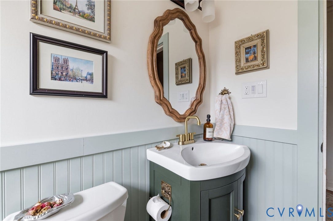 Pedestal sink with brass faucet, set against beadboard paneling and a decorative mirror