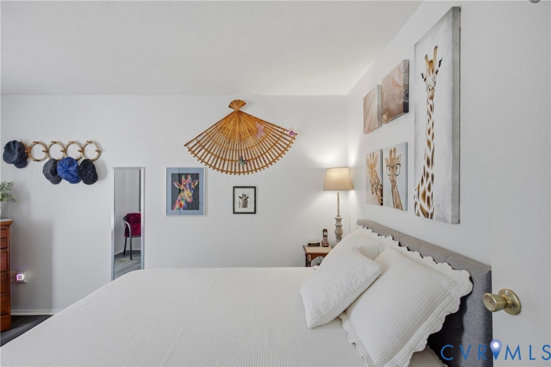 2007 Mountain Pine Boulevard, Three Pines, Richmond, VA 23235 Serene primary bedroom showcasing crisp white bedding, soft ambient lighting from an integrated table lamp, and curated wall art