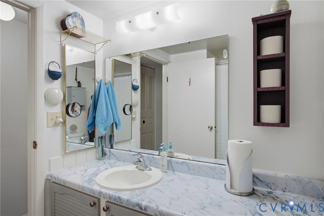 2007 Mountain Pine Boulevard, Three Pines, Richmond, VA 23235 Spa-inspired bathroom featuring a large framed mirror, marble-look countertop with an integrated sink basin, polished chrome faucet fixtures, and ample storage cabinetry