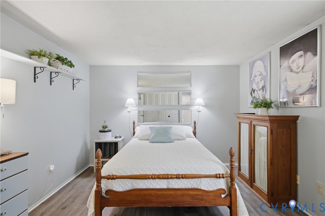 2007 Mountain Pine Boulevard, Three Pines, Richmond, VA 23235 Bright, light-filled bedroom featuring hardwood flooring, a wood-frame bed with brass accents, and soft ambient lighting from dual wall-mounted sconces