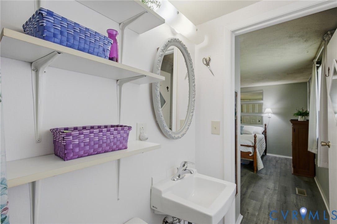 2007 Mountain Pine Boulevard, Three Pines, Richmond, VA 23235 Compact bathroom featuring white subway tile walls, floating shelves with storage, an oval mirror with chrome frame, and a pedestal sink