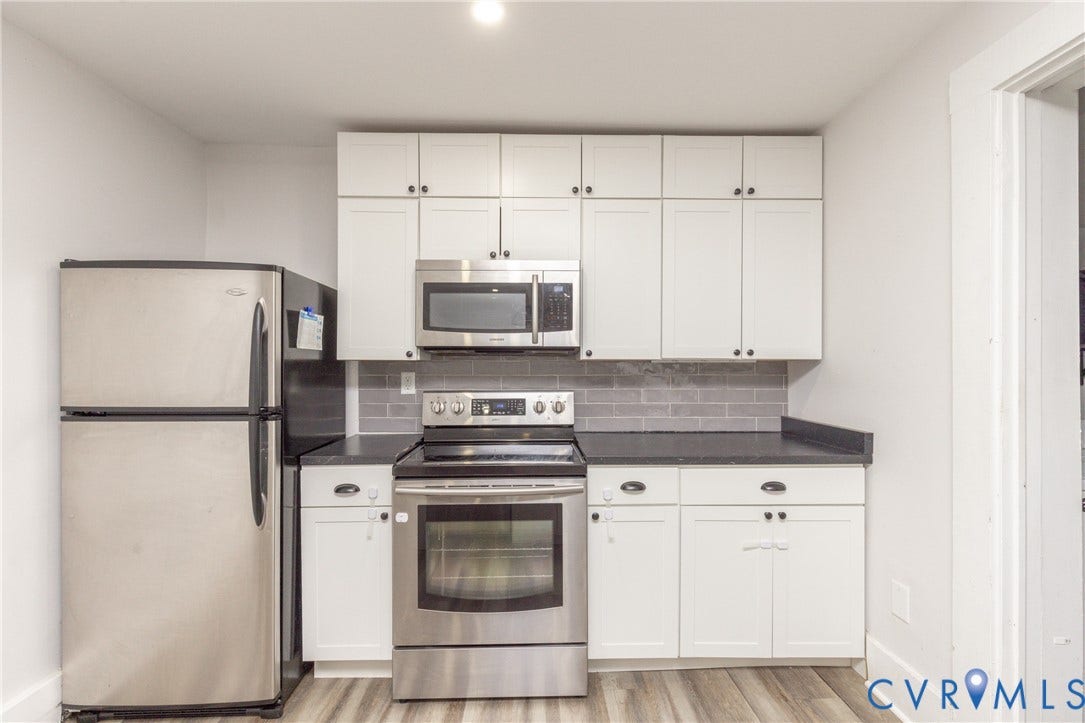 716 E Gladstone Avenue, Richmond, VA 23222 Stainless steel appliances, white cabinetry, dark countertops, subway tile backsplash, and wood-finish flooring