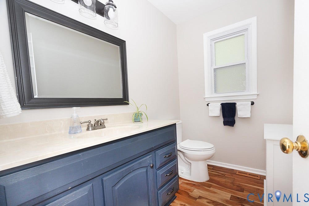 419 Rossmere Drive, Walton Park, Midlothian, VA 23114 Bathroom featuring a navy blue vanity with a light-colored countertop, a rectangular framed mirror, wood-finish flooring, a toilet, and a window with white trim