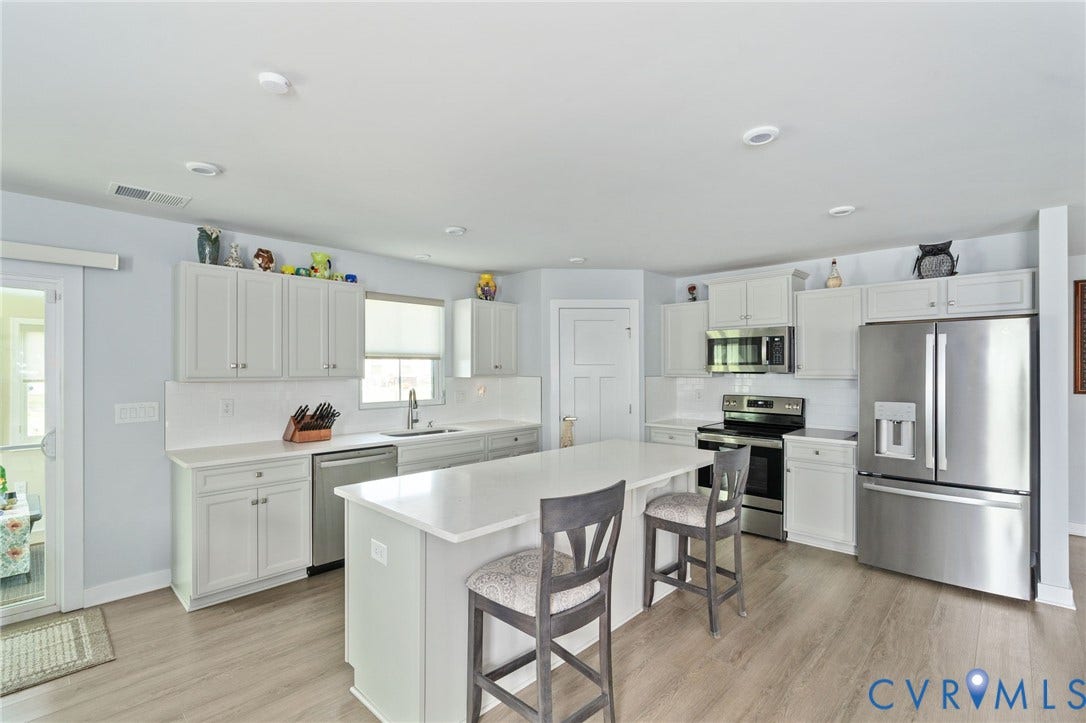 7484 Southamptonshire Way, Autumn Pines, New Kent, VA 23124 Kitchen featuring a large island with seating, stainless steel appliances, white cabinetry, quartz countertops, and a white subway tile backsplash