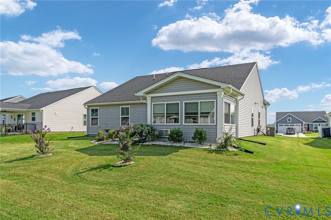 7484 Southamptonshire Way, Autumn Pines, New Kent, VA 23124 Rear exterior featuring a sunroom addition with large windows, light gray siding, dark shingle roofing, and a manicured lawn