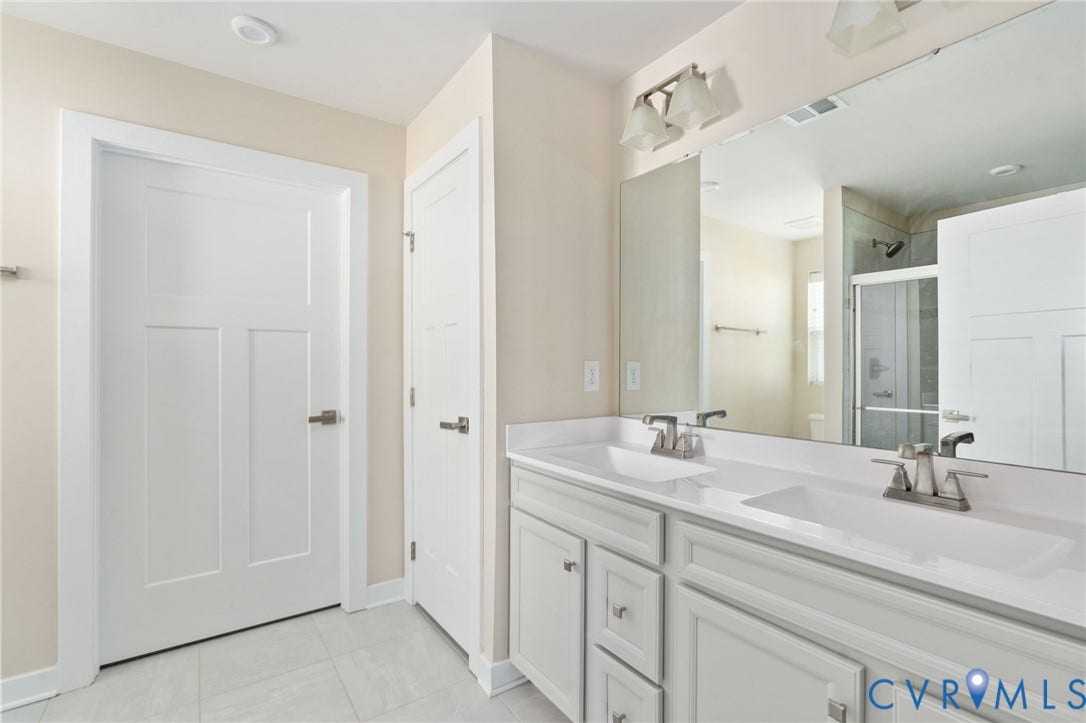 7484 Southamptonshire Way, Autumn Pines, New Kent, VA 23124 Bathroom featuring a dual vanity with white countertops, white cabinetry, a large mirrored wall, tile flooring, and a glass-enclosed shower