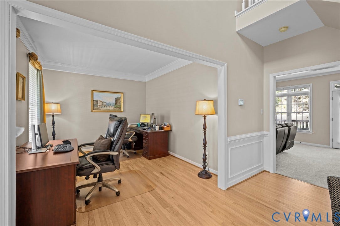 Light wood-finish flooring extending from the entryway into a room with crown molding and a window featuring blinds and a valance
