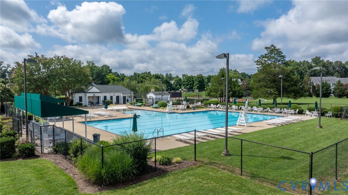 Outdoor swimming pool featuring multiple lap lanes, a surrounding concrete deck, and ample lounge seating