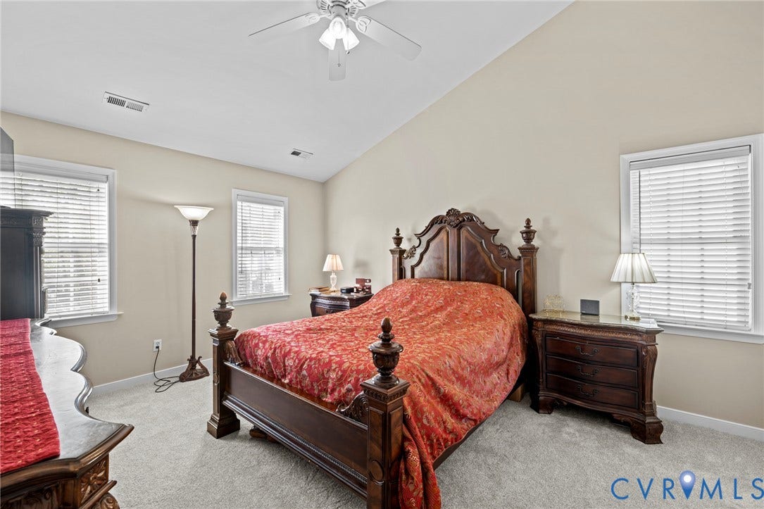 Carpeted room featuring a vaulted ceiling with a ceiling fan, two windows with blinds, and neutral-toned walls