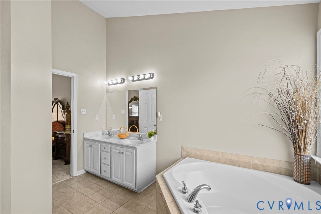 Bathroom featuring a built-in soaking tub, dual vanity with white cabinetry, tile flooring, and vaulted ceiling