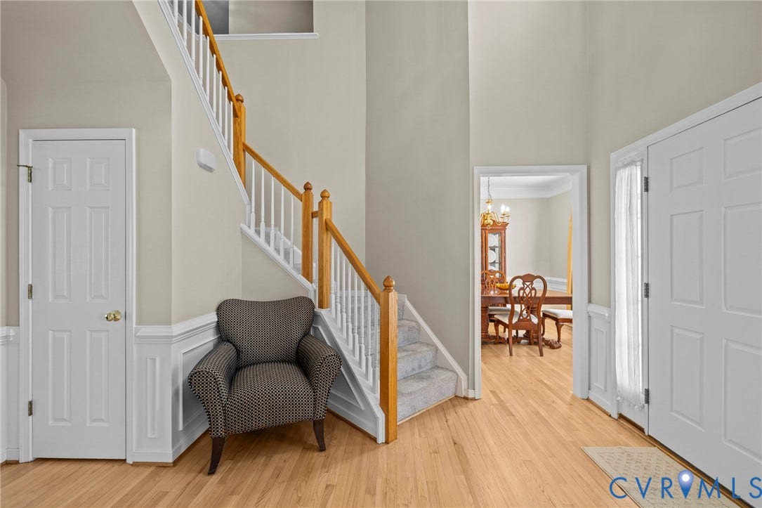 Entryway featuring wood-finish flooring, wainscoting, a multi-story ceiling, a carpeted staircase with wood handrails, and a paneled front door with side window