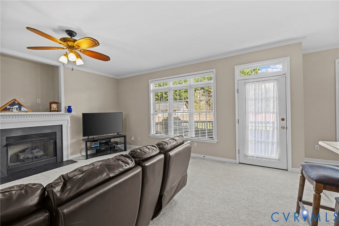 Carpeted living space featuring a fireplace with a white mantel, an overhead ceiling fan, and a glass-paneled exterior door