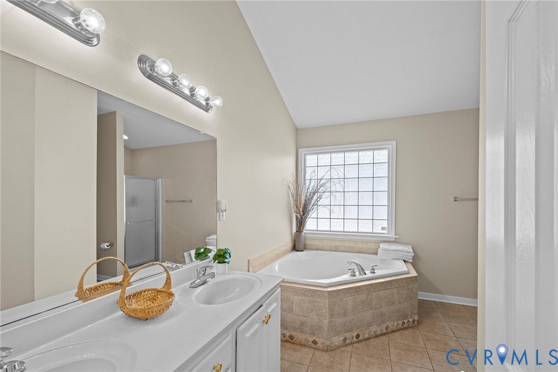 Bathroom featuring a tiled corner soaking tub with a frosted grid window, dual vanity with undermount sinks, wall-mounted light fixtures, and a glass-enclosed shower