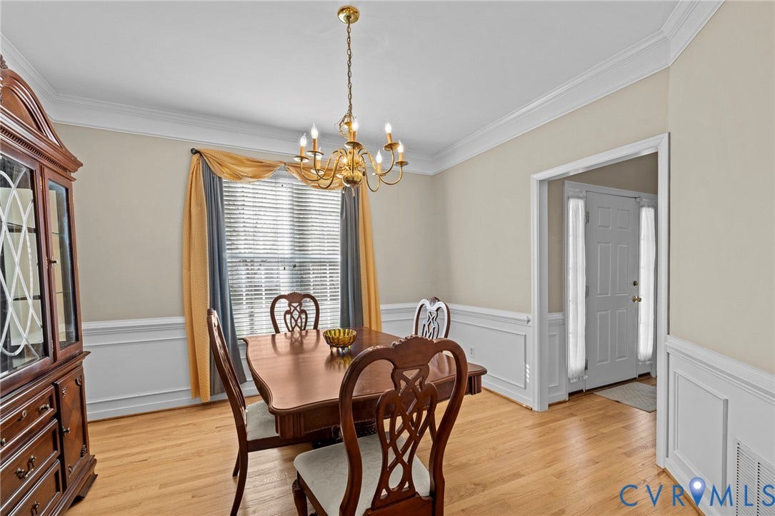 Dining area featuring wood-finish flooring, white wainscoting, crown molding, and a brass chandelier