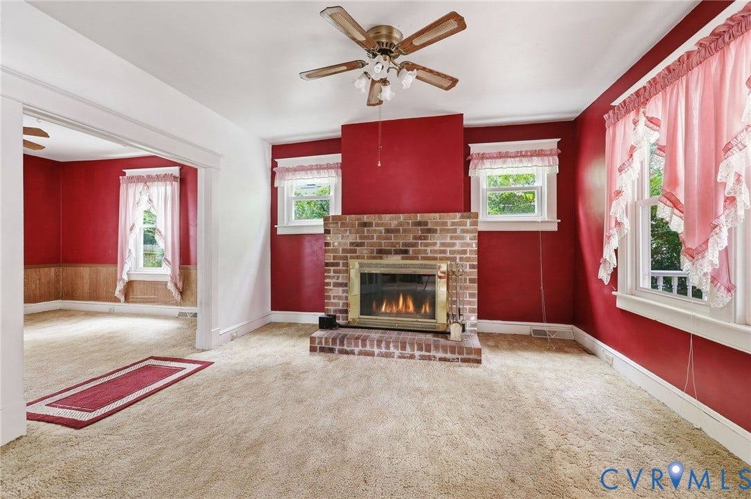 Living area featuring a brick fireplace with a brass firebox, ceiling fan, and carpeted flooring