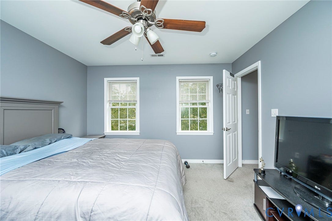 11821 Park Forest Way, Glen Allen, VA 23059 Bedroom featuring light gray walls, two windows with white trim, a ceiling fan with wood-finish blades, and neutral carpeting