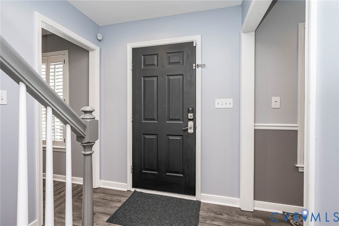 11821 Park Forest Way, Glen Allen, VA 23059 Entryway featuring a dark paneled door with modern hardware, wood-finish flooring, and a gray-painted staircase with white spindles