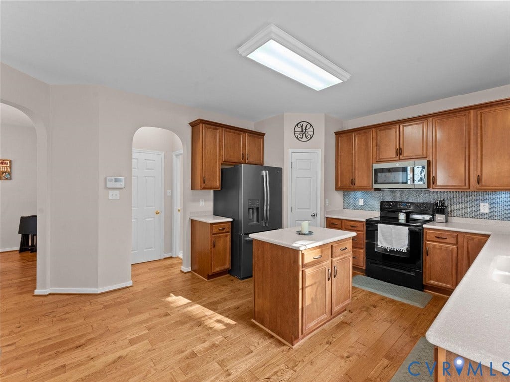 2606 Water Race Terrace, Watermill, Midlothian, VA 23112 Kitchen featuring wood-finish flooring, an island with storage, light-toned countertops, a patterned tile backsplash, and wood cabinetry