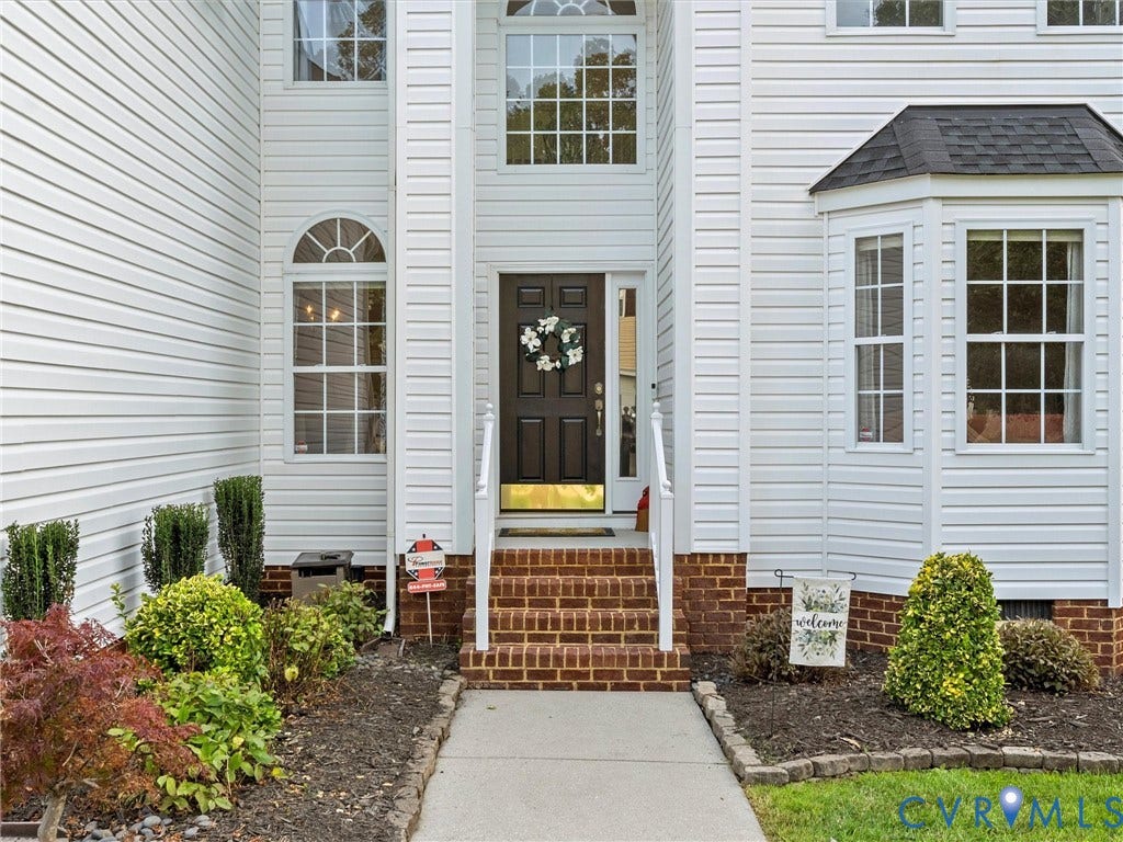 2606 Water Race Terrace, Watermill, Midlothian, VA 23112 White vinyl siding exterior with a dark entry door, brick foundation, bay window, arched window, and mature landscaping