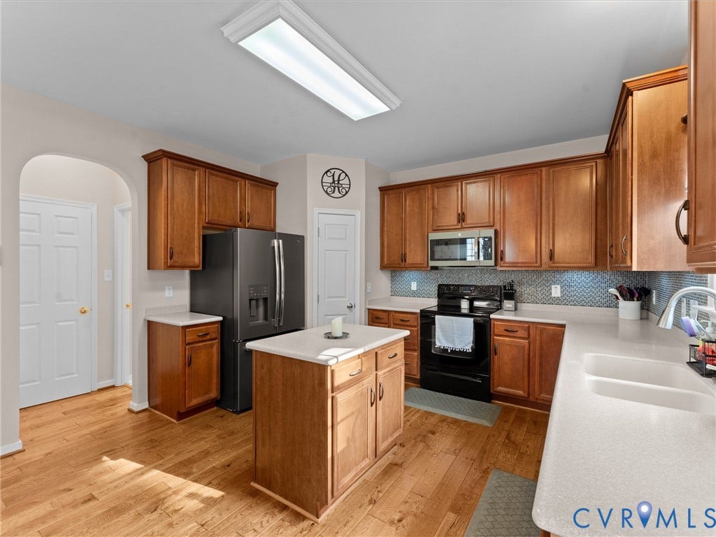 2606 Water Race Terrace, Watermill, Midlothian, VA 23112 Kitchen featuring wood-finish flooring, a central island, light-toned countertops, a herringbone tile backsplash, and wood cabinetry