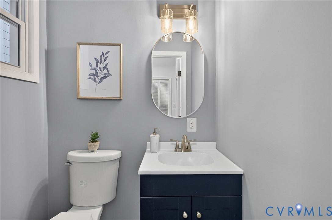 526 N 33rd Street, Church Hill, Richmond, VA 23223 Half Bath, First floor, Oval vanity mirror, brushed nickel faucet, single basin sink, white countertop, and dark blue vanity cabinetry with chrome hardware